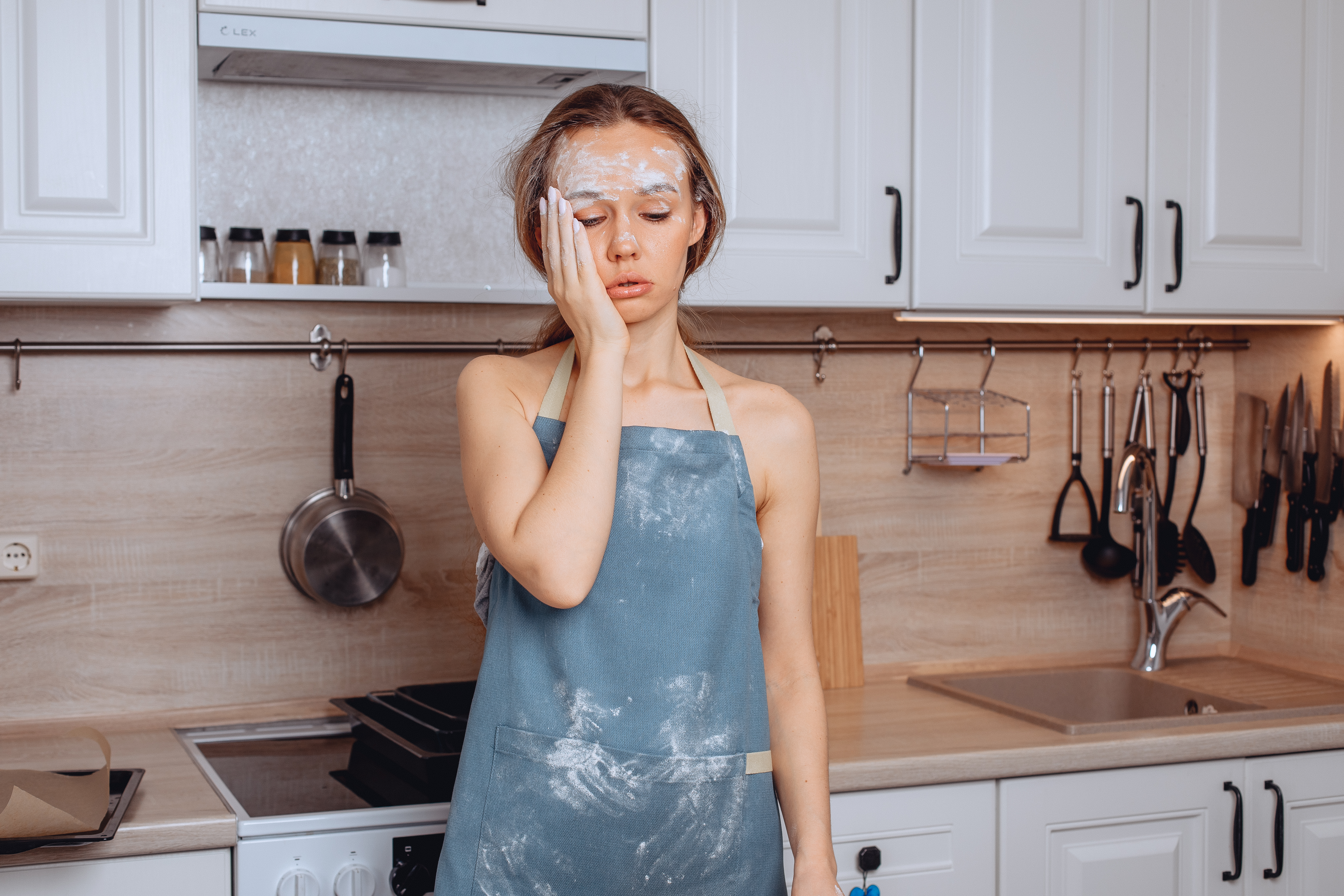 picture-girl-slightly-stained-with-blue-flour-aprons-standing-kitchen-putting-her-head-her-face-feeling-fatigue-from-long-prolonged-cooking-whole-forehead-is-covered-flour